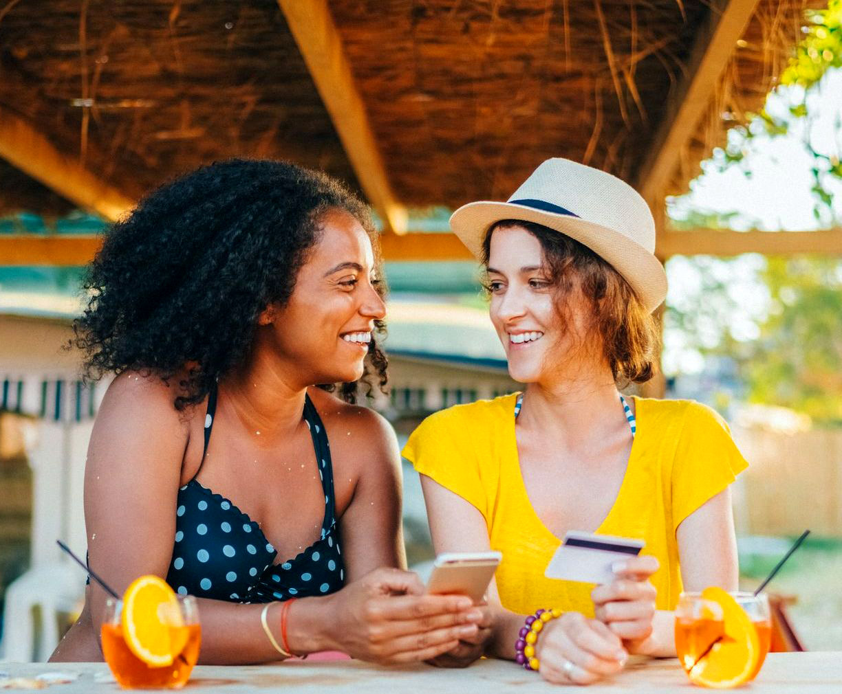 Two women sitting outside looking at a Dover Federal Credit Union savings account on a smart phone while enjoying drinks with lemon wedges and straws.