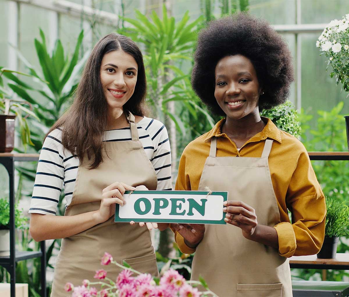 Two woman hold an open for business sign